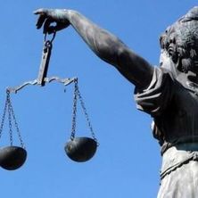 Justitia mit Wage in der Hand von schräg hinten vor blauem Himmel